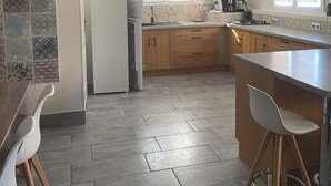 A kitchen with wooden cabinets, a tiled backsplash, and a bar area with stools. - Country house (Malataverne)