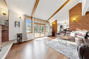 Ein geräumiges Wohnzimmer mit Kamin aus Ziegelsteinen, einer Ledersofa und großen Fenstern.