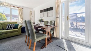 Et værelse med et spisebord, stole, en sofa og et stort vindue med gardiner.