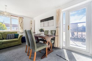 Een kamer met een eettafel, stoelen, een bank en een groot raam met gordijnen.