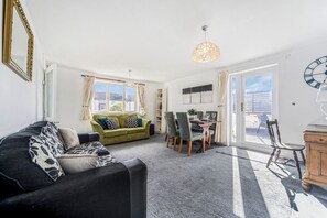 Ein Wohnzimmer mit einer Couch, einem Esstisch mit Stühlen, einer Chandelüster und Blick durch die Glastür.