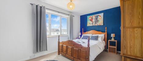 Un dormitorio con una cama de madera, una ventana con cortinas, una pared azul y un cuadro.
