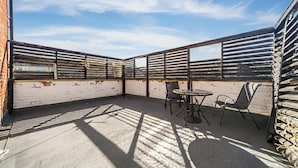 En udendørs terrasse med et bord og stole, en murstensmur og en klar himmel.