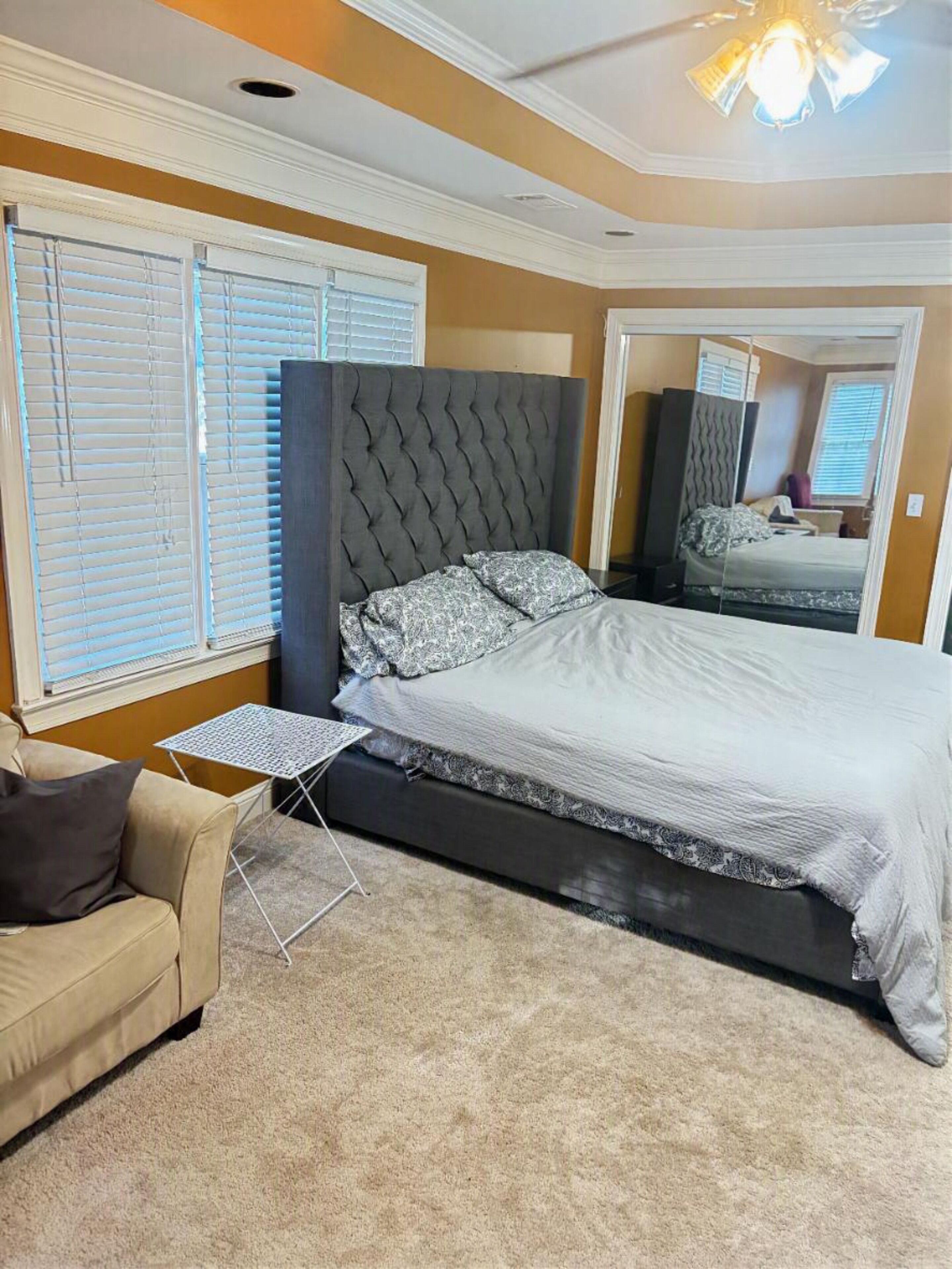 A bedroom with a bed, a small table, a sofa, and a mirror.