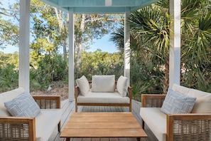 Ein überdachter Außenbereich mit einem Holztisch, zwei Korbuschesel mit Kissen und einer Pergola.