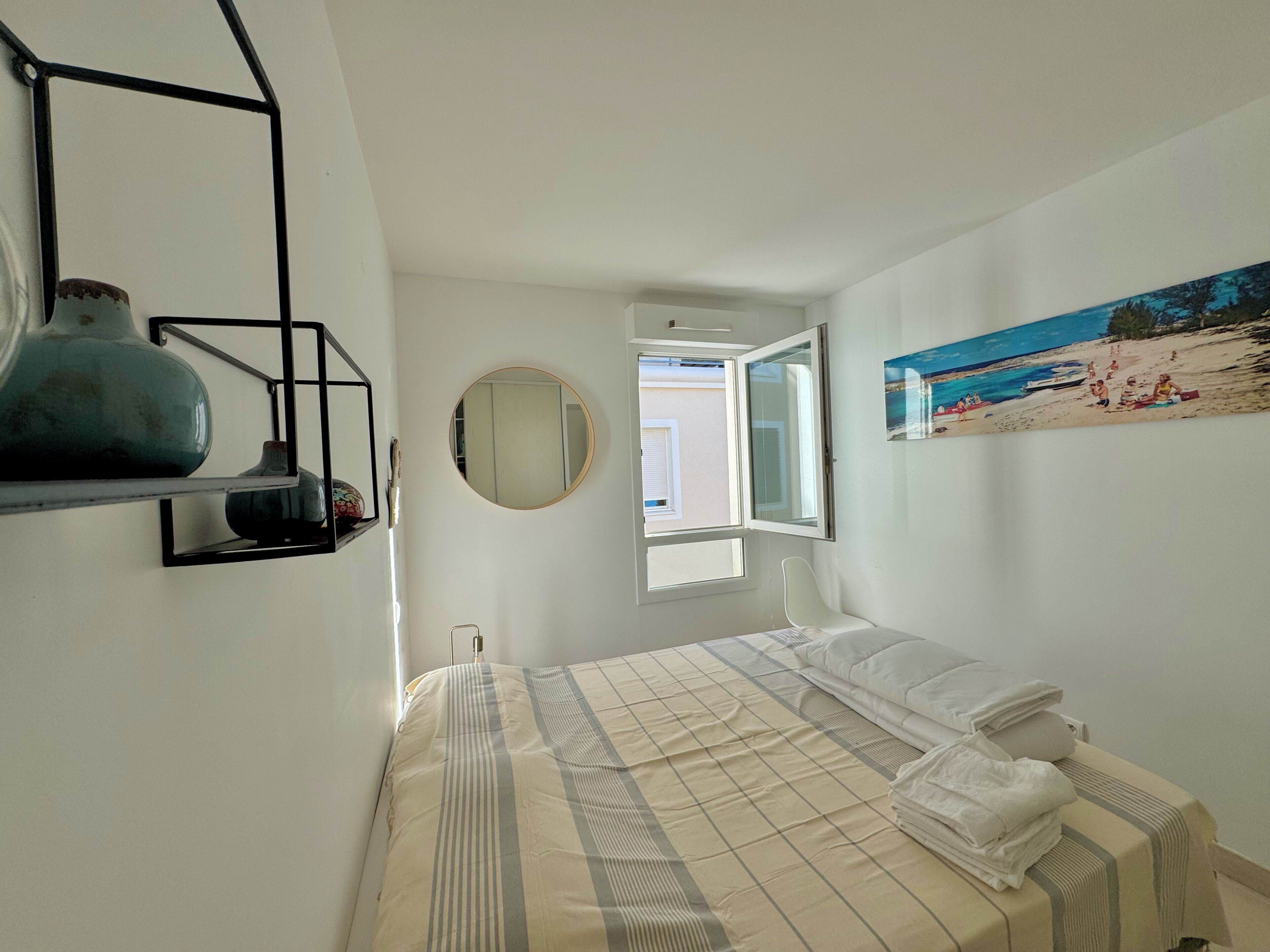 Ein Schlafzimmer mit einem Bett, einem runden Spiegel, einem Fenster und einem Bild an der Wand.