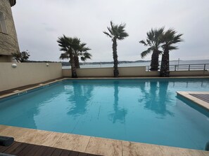 A swimming pool with palm trees and a view of the sea. - L'Écrin Bleu BANDOL: A Magnificent Apartment with a Panoramic View of the Mediterranean (Bandol)
