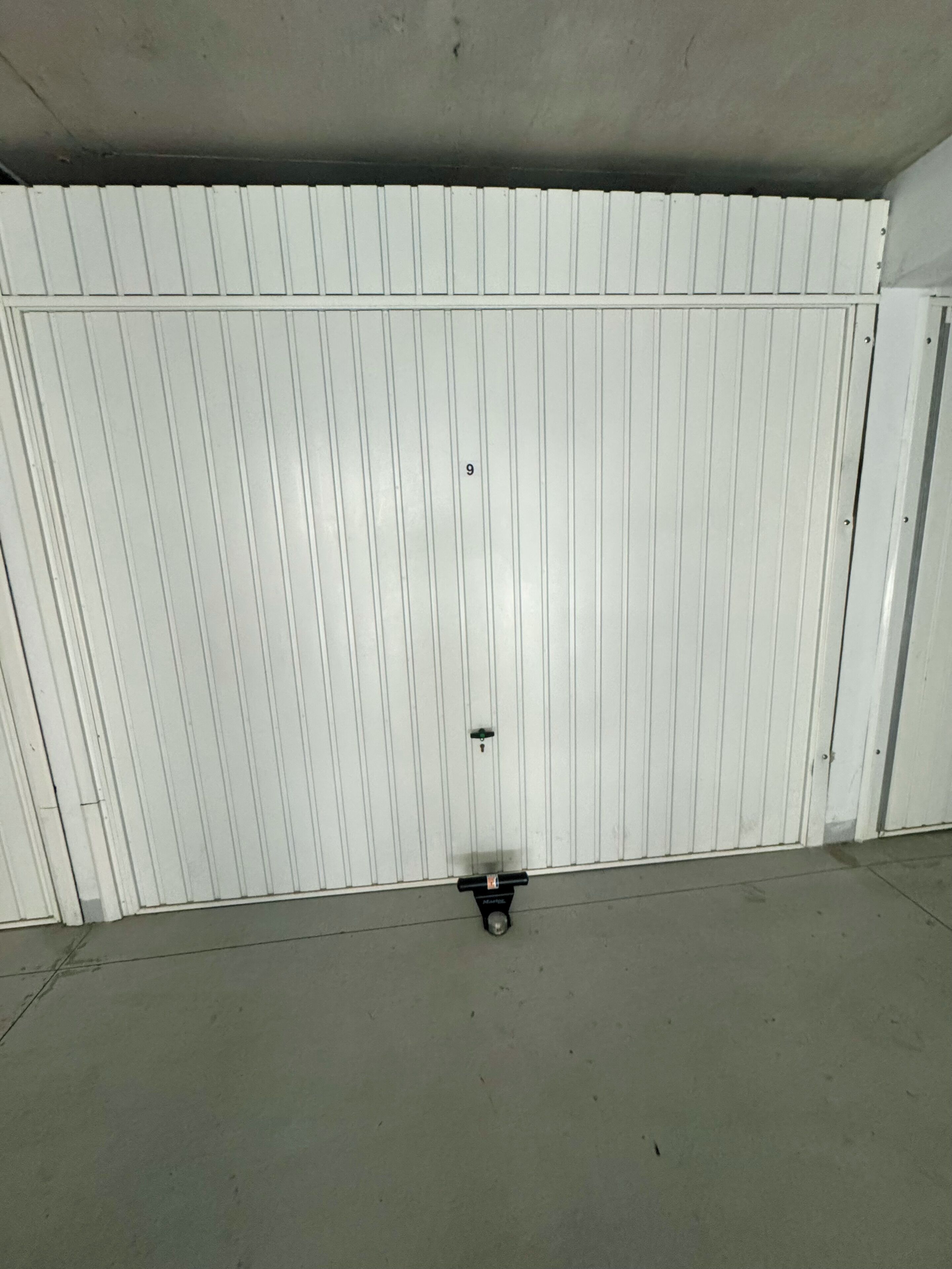 Een witte, gesloten metalen deur met een klein, zwart voorwerp op de vloer.
