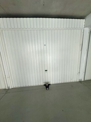 Eine weiße, geschlossene Metalttür mit einem kleinen, schwarzen Gegenstand auf dem Boden.