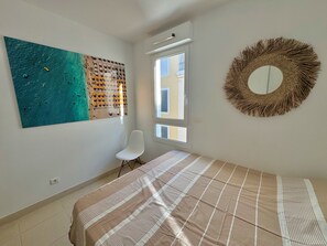 Ein Schlafzimmer mit einem Bett, einem Sessel, einem großen abstrakten Gemälde, einem Fenster und einer Wanddekoration aus Textil.