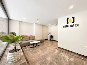 Un interior moderno con un sofá, una mesita, una planta en maceta, un dispensador de agua y una pared con el logotipo 'NIKOMIX'.