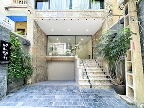 A building entrance with a stone facade, a glass door, and a small outdoor area with steps and potted plants. - Hannari Cozy Serviced Apartment (Hanoi)