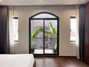 Un dormitorio con un ventanal grande, una cama y dos plantas en macetas.
