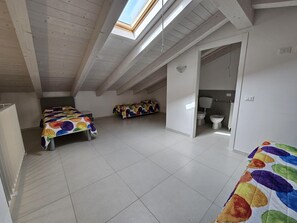 A spacious attic bedroom with a skylight, two beds with colorful bedding, a bathroom with a toilet and bidet, and a white tiled floor. - Appartment in Rosolina Mare (Rosolina)