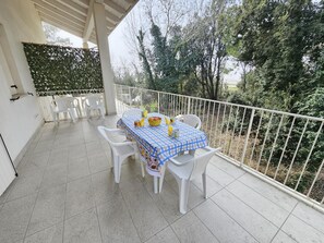 A covered outdoor patio with a table set for two, surrounded by white plastic chairs, and a white railing. - Appartment in Rosolina Mare (Rosolina)