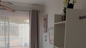 Ein Schlafzimmer mit Bett, Kleiderschrank, Vorhang, Wandleuchte und Fenster mit Blick auf einen Zaun und ein Gebäude.
