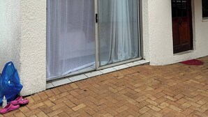 Ein Gebäude mit weißer Fassade, einer Schiebetür mit weißem Vorhang, einem grünen Vordach und einem von Ziegeln gepflasterten Vorplatz.