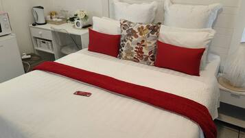 A neatly made bed with white and red bedding, a small bedside table with a lamp, and a white wall with a framed picture.
