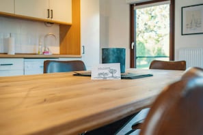 Une table de salle à manger en bois, ornée d’une pancarte « BIENVENUE », d’un vase foncé et d’une fenêtre donnant sur des arbres.
