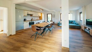 Una cocina moderna con comedor, suelo de madera y sala de estar con sofá y televisor.