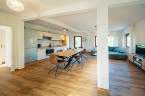 Eine moderne Küche mit Essbereich, Holzboden und einem Wohnzimmer mit Sofa und Fernseher.
