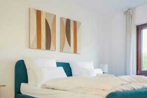 Un lit bien fait, avec une literie blanche, une tête de lit turquoise et deux œuvres d’art abstraites accrochées au mur.