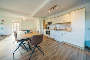 Une cuisine moderne avec des meubles blancs, une table à manger en bois et un four encastré.
