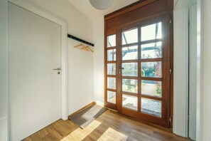 Une pièce avec un plancher en bois, une porte blanche et une grande fenêtre à carreaux.