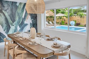 A dining area with a table set for six, a large vase, and a view of a pool and outdoor seating. - Resort Escape | Pool, Tiki, Hammock & Cold Plunge (Plantation)