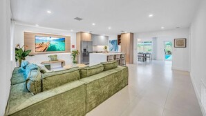 Een moderne woonkamer met een groene bank, een flatscreen-tv en een keuken met een koelkast en kastjes.