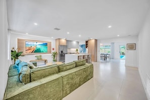 Ein modernes Wohnzimmer mit einem grünen Sofa, einem Flachbildfernseher und einer Küchenzeile inklusive Kühlschrank und Schränken.