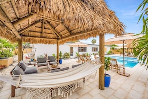 A covered outdoor seating area with a hammock, lounge chairs, and a pool in the background. - Resort Escape | Pool, Tiki, Hammock & Cold Plunge (Plantation)