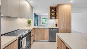 Een moderne keuken met houten kastjes, een inbouwoven, een vaatwasser en een koffiehoek.