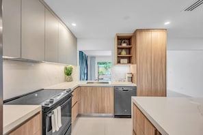 A modern kitchen with wooden cabinets, a built-in oven, a dishwasher, and a coffee bar. - Resort Escape | Pool, Tiki, Hammock & Cold Plunge (Plantation)