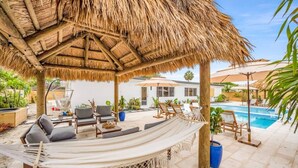 A covered outdoor seating area with a hammock, lounge chairs, and a pool in the background. - 2 Resort Homes Side-by-Side - Pool, Tiki, Ice Bath (Plantation)
