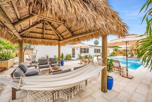 A covered outdoor seating area with a hammock, lounge chairs, and a pool in the background. - 2 Resort Homes Side-by-Side - Pool, Tiki, Ice Bath (Plantation)
