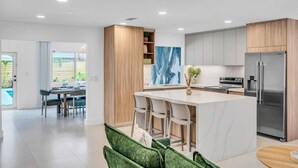 A modern kitchen with a central island, stainless steel appliances, and a dining area with chairs. - 2 Resort Homes Side-by-Side - Pool, Tiki, Ice Bath (Plantation)
