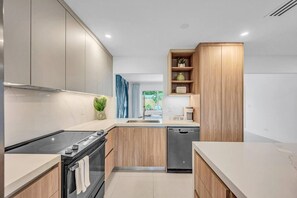 A modern kitchen with wooden cabinets, a built-in oven, a dishwasher, and a coffee bar. - 2 Resort Homes Side-by-Side - Pool, Tiki, Ice Bath (Plantation)