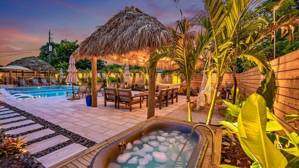 A pool area with a hot tub, lounge chairs, and a thatched-roof structure. - 2 Resort Homes Side-by-Side - Pool, Tiki, Ice Bath (Plantation)