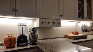 Een keuken met witte kastjes, een blender, een mixer en een fruitschaal op het aanrecht.