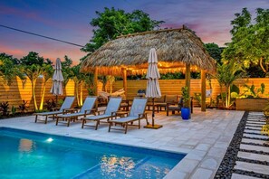 A poolside area with lounge chairs, a thatched gazebo, and a wooden fence. - Island Vibe`s Retreat | Pool, Tiki & Cold Plunge (Plantation)