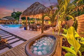Et poolområde med jacuzzi, liggestole og en struktur med stråtæthed.