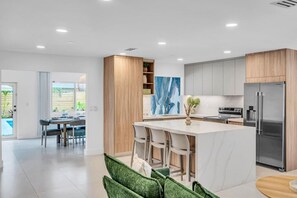 A modern kitchen with a central island, stainless steel appliances, and a dining area with a view of the outdoors. - Island Vibe`s Retreat | Pool, Tiki & Cold Plunge (Plantation)