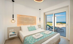 Ein modernes Schlafzimmer mit einem großen Bett, einer Wand aus Stein, Meerblick durch eine Schiebetür und einem kleinen Nachttisch mit einem Buch und einer Tasse.