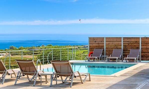 Ein Poolbereich mit Liegestühlen und Blick auf das Meer.