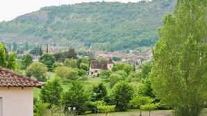 A rural setting with a house surrounded by greenery and a hill in the background. - Lovely Duplex With Scenic Terrace (Carayac)
