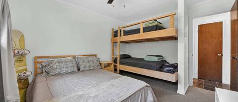 A room with a bunk bed, a single bed, a ceiling fan, a door, and a small table.