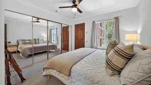 Een slaapkamer met een bed, een plafondventilator, een grote spiegel en uitzicht op een andere kamer.