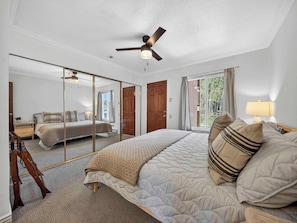 Ein Schlafzimmer mit Bett, Deckenventilator, großem Spiegel und Blick auf einen anderen Raum.