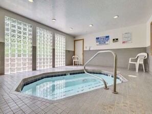 Ein Hallenbad mit großen Glaswänden, Fliesenboden und einem Rettungsschwimmerstand.